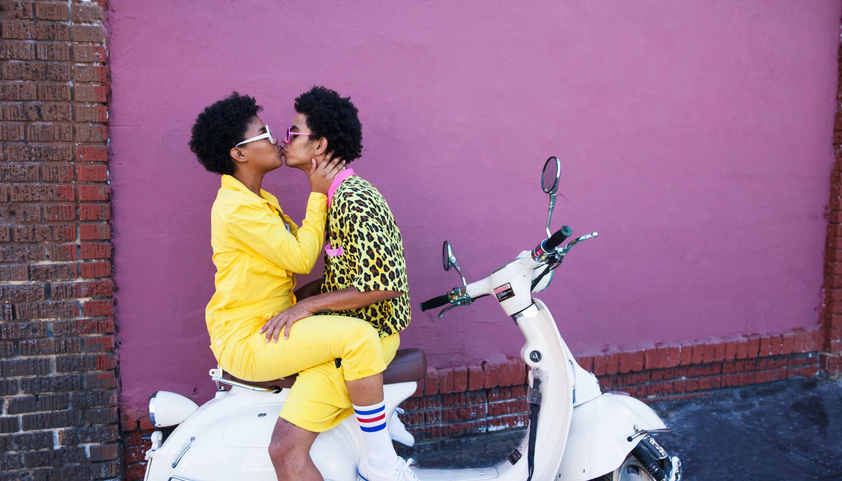 A young couple wearing yellow outfits sitting on a scooter kissing