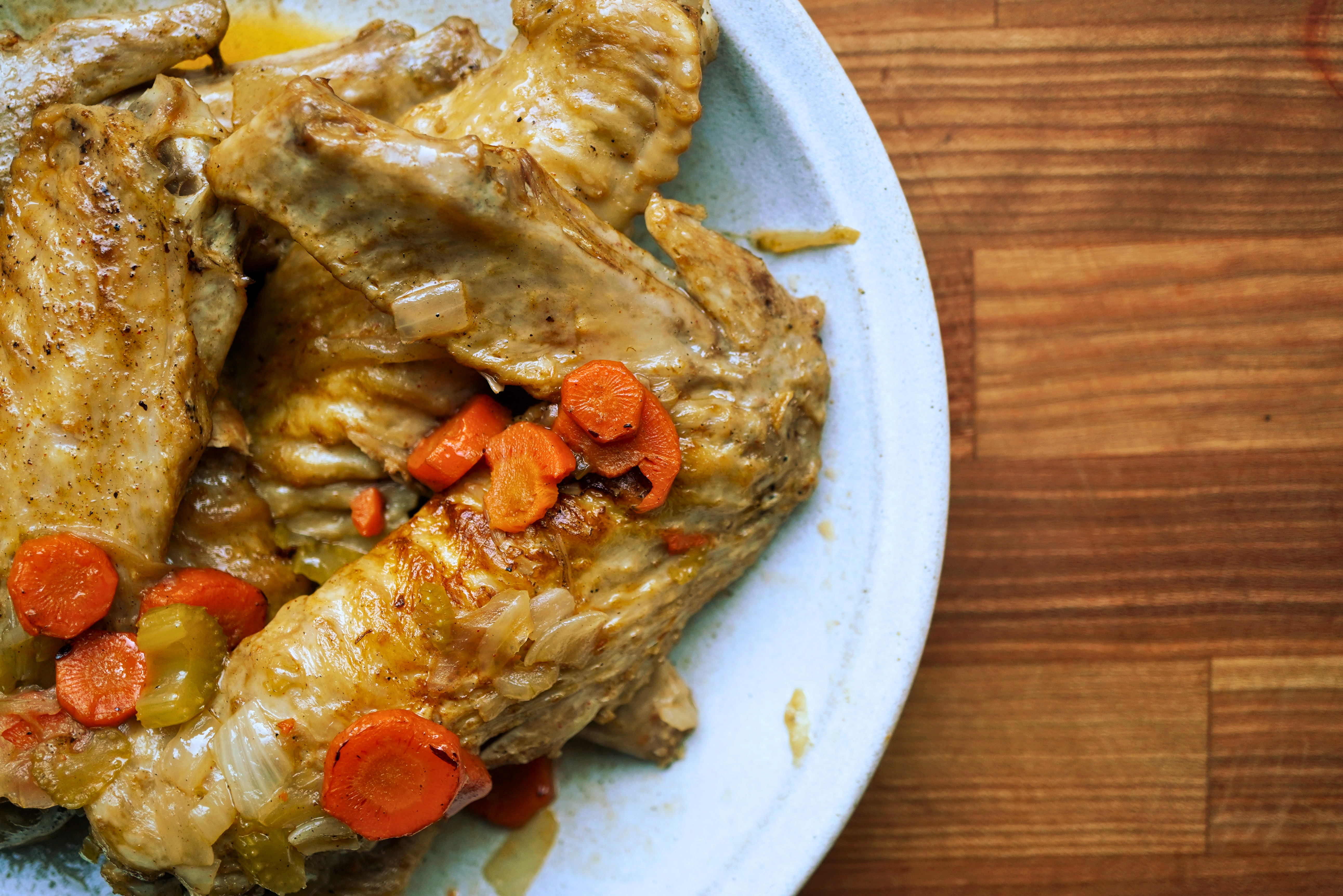 A plate of braised meat and vegetables, including carrots and celery, on a wooden table.