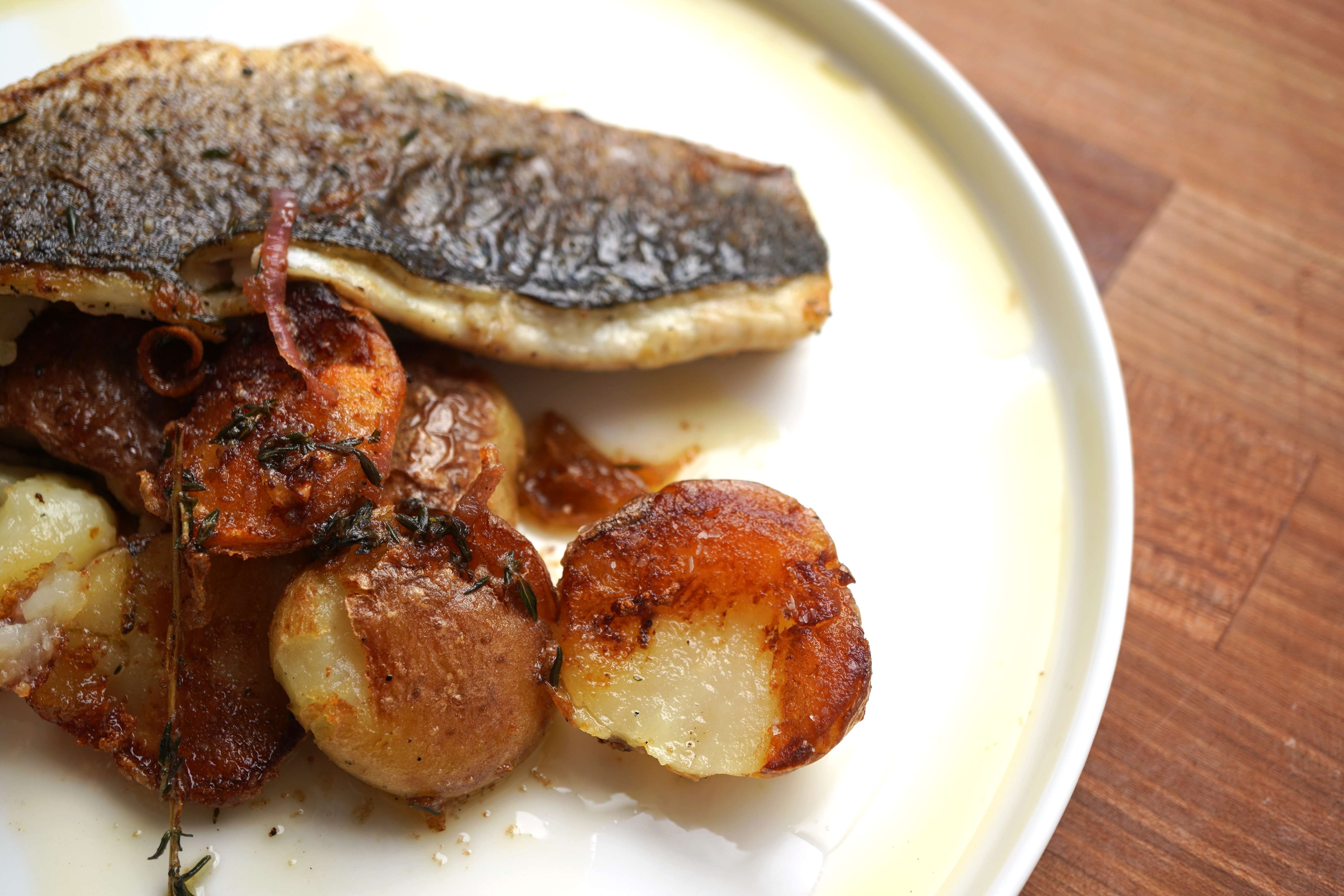 A plate of roasted meat and potatoes, with a crispy skin on the meat and golden brown potatoes.