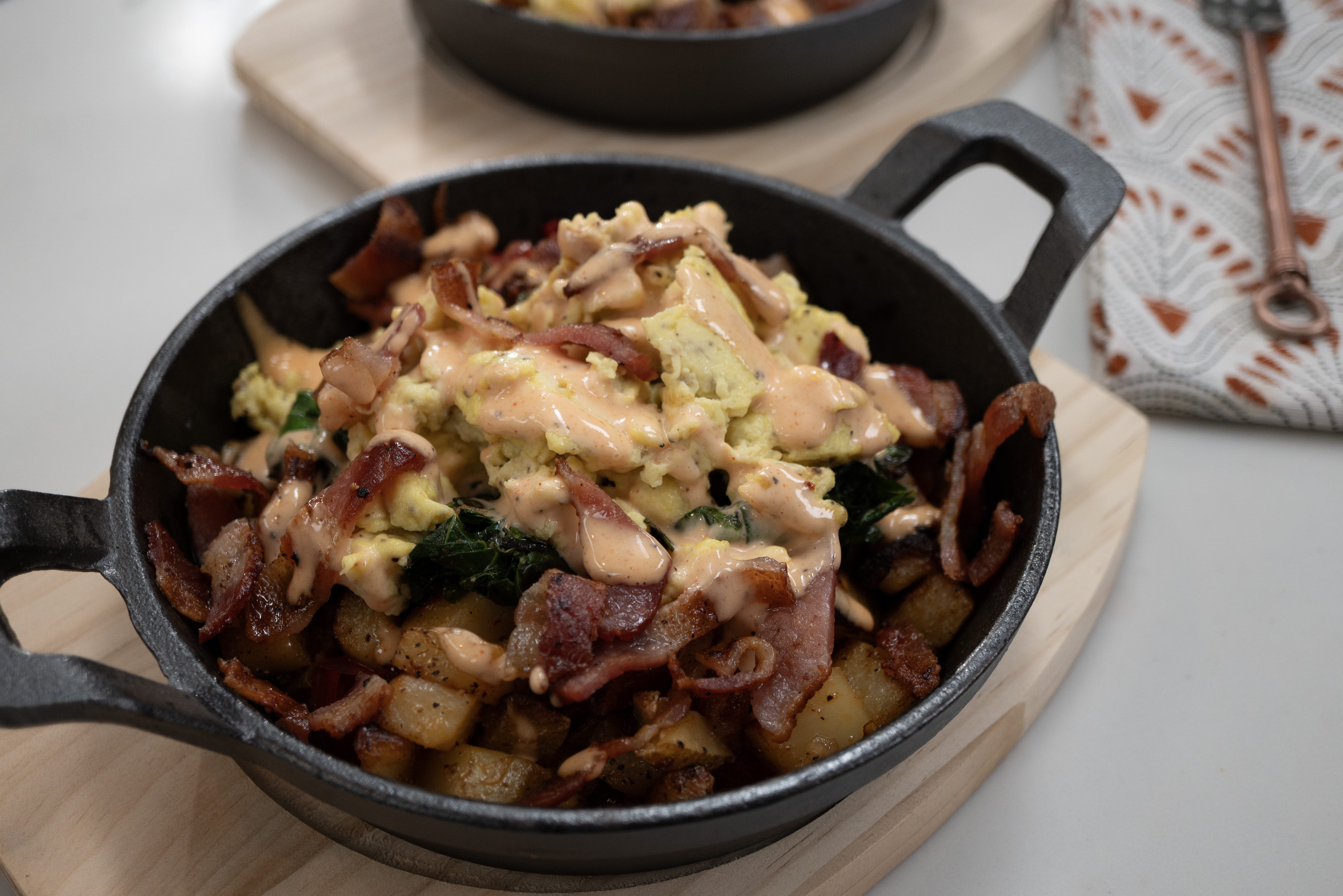 A cast iron skillet filled with a hearty breakfast dish of scrambled eggs, bacon, and potatoes.