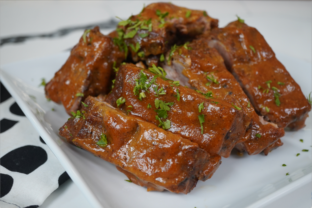 Plate of braised pork ribs in a sweet and savory sauce, garnished with fresh parsley.