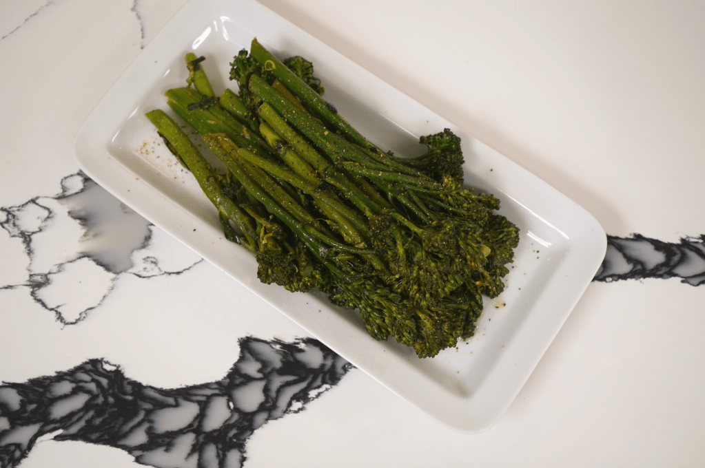 Plate of roasted green vegetables, including asparagus and broccoli, on a white plate against a black and white marble background.