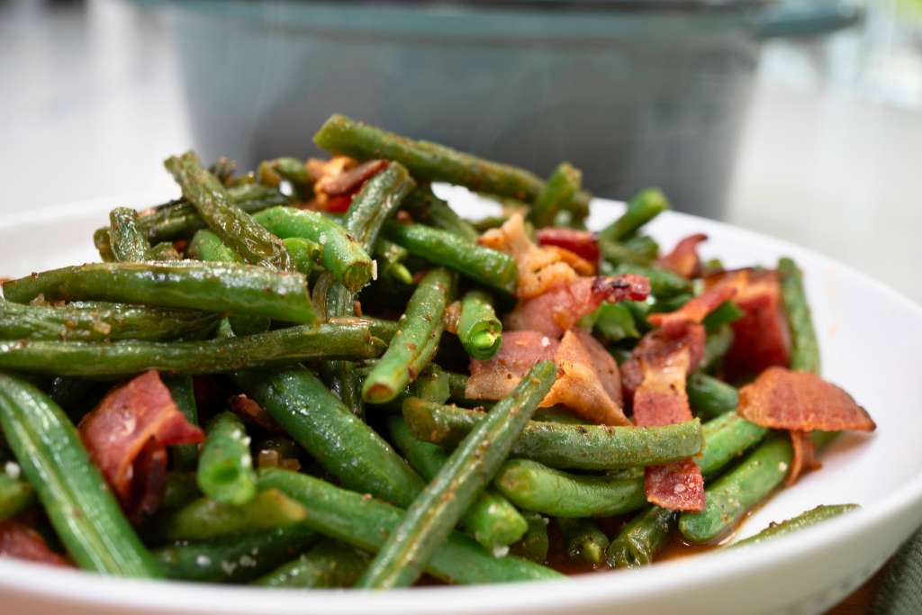A plate of sautéed green beans and bacon pieces.