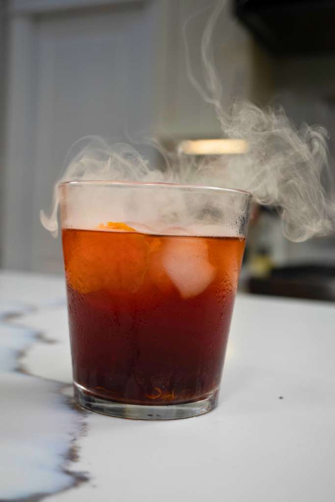 A glass of iced coffee or tea with steam rising from it, against a light background.