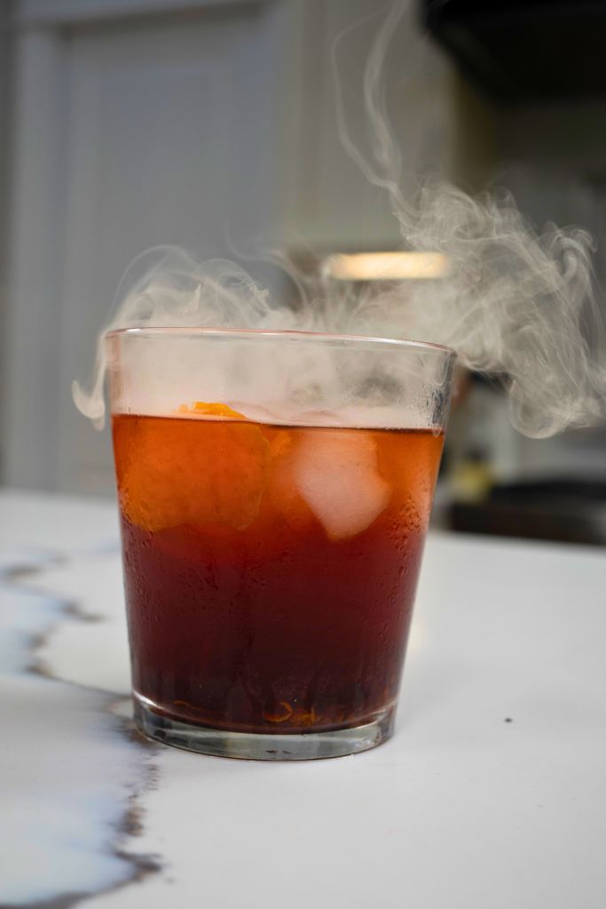 A glass of iced coffee or tea with steam rising from it, against a light background.