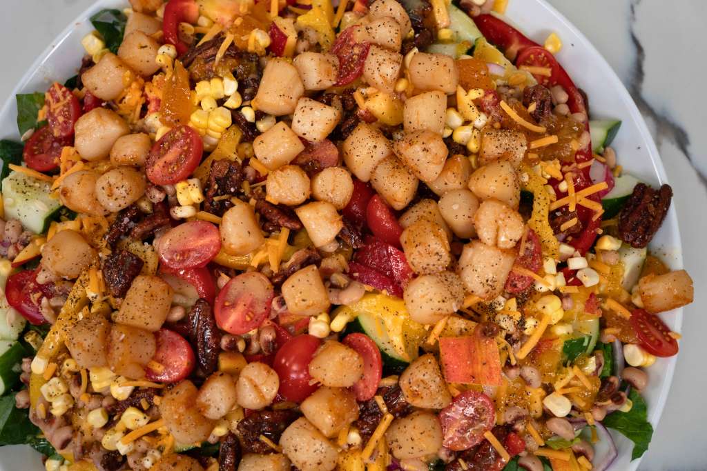 A plate of mixed vegetables, including corn, tomatoes, and potatoes, seasoned with spices and served on a bed of greens.