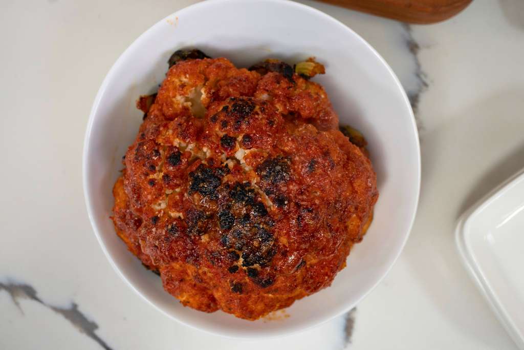 A white bowl filled with a spicy, tomato-based dish, possibly a curry or stew, with visible charred or blackened spots on the surface.
