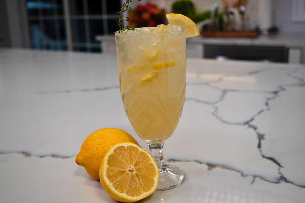 A glass of lemonade garnished with a lemon slice on a marble countertop.
