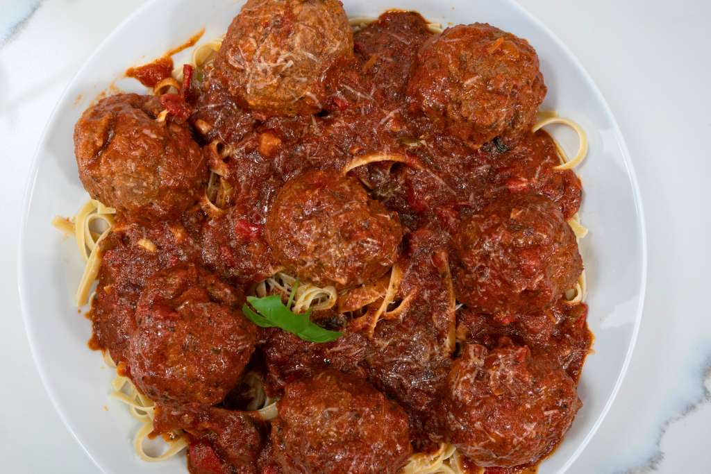 Plate of spaghetti and meatballs in a rich tomato sauce, garnished with a fresh green herb.