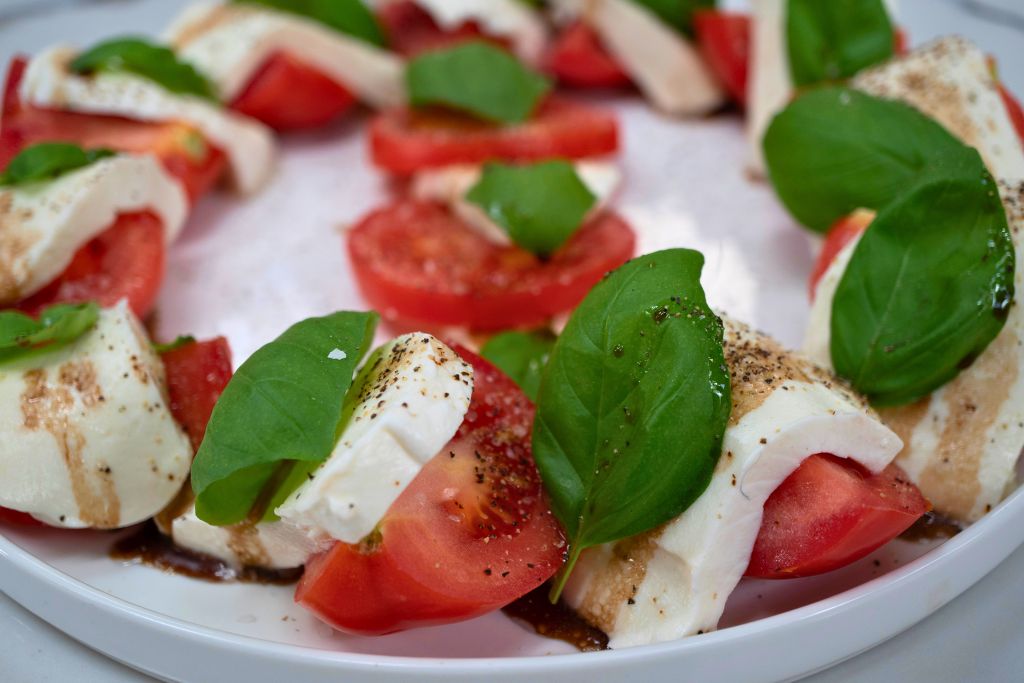 A plate of fresh tomato slices, mozzarella cheese, and basil leaves, seasoned with olive oil and balsamic vinegar.