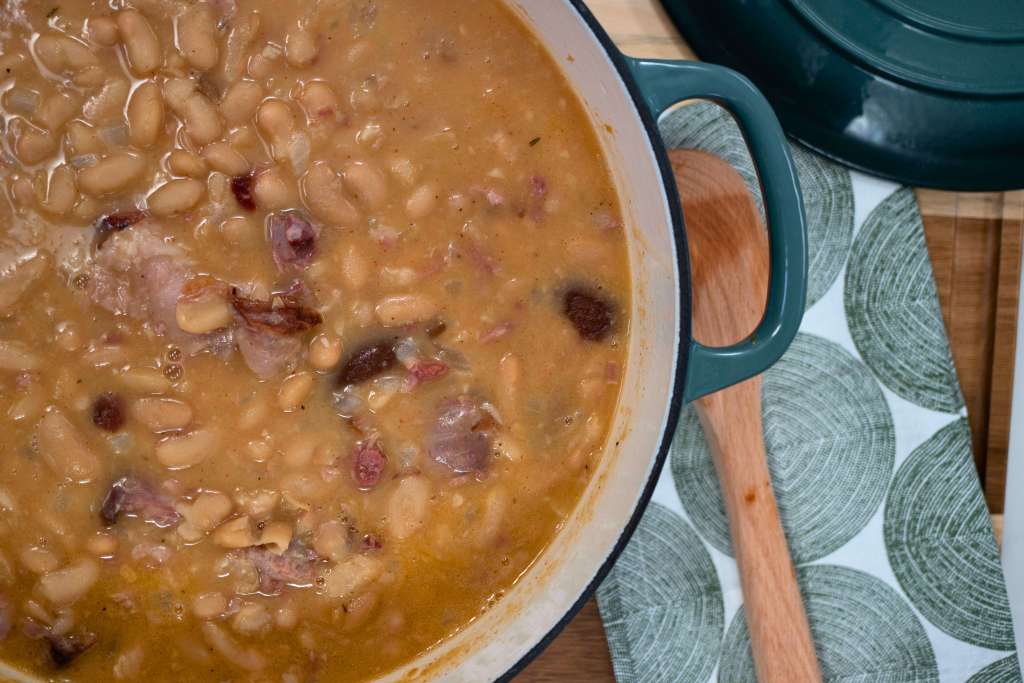 A pot of hearty bean soup with visible chunks of meat and vegetables simmering on a wooden surface.