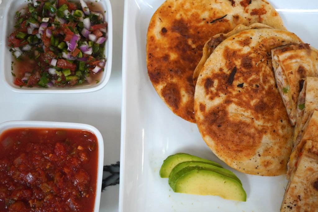 Assorted Mexican dishes including tortillas, salsa, and avocado slices on a white plate.