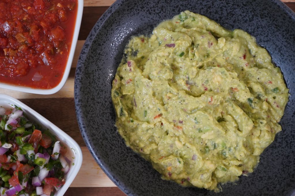 A plate of guacamole and a bowl of salsa on a wooden table.