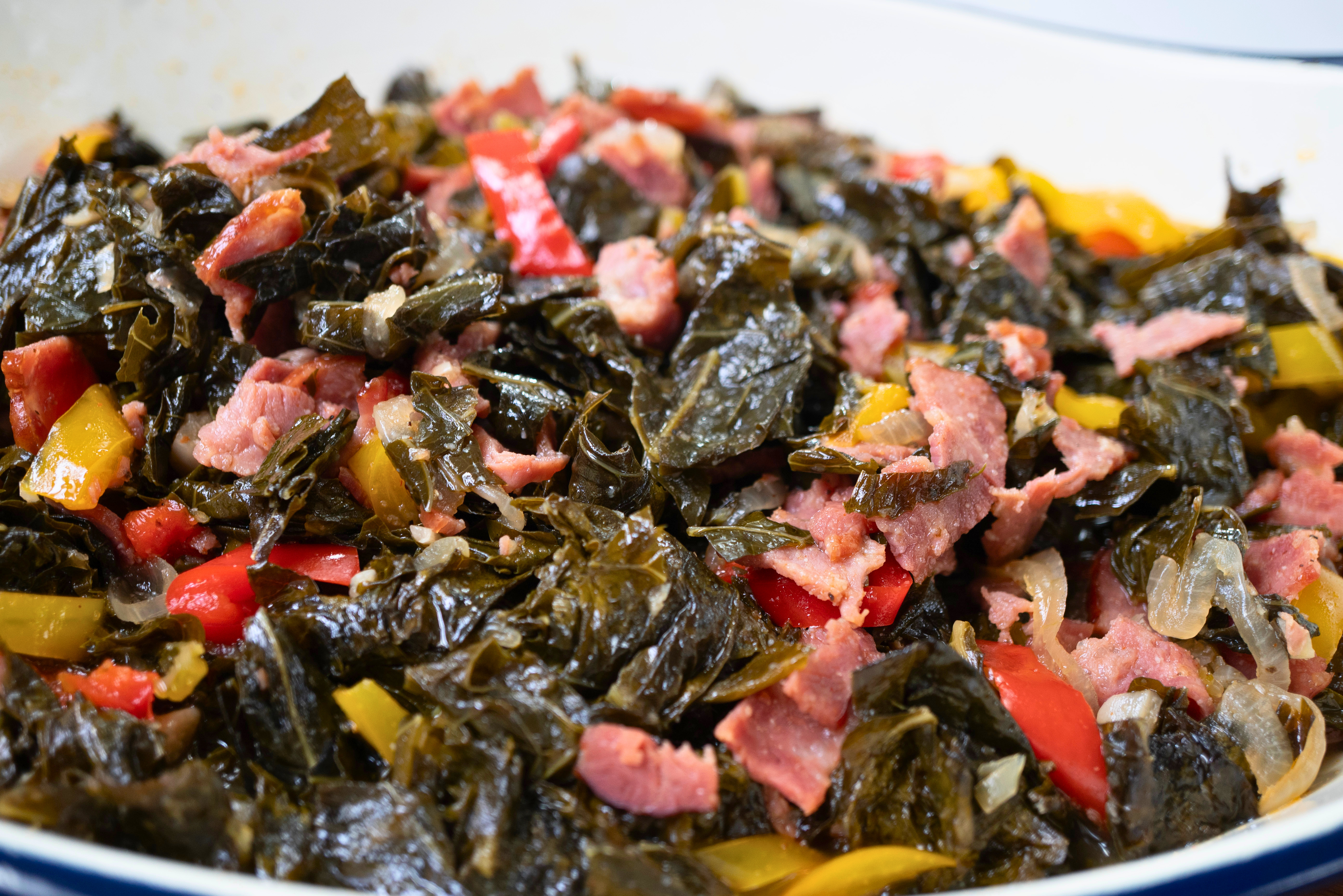 A plate of cooked greens and meat, including kale, peppers, and what appears to be ham or bacon.