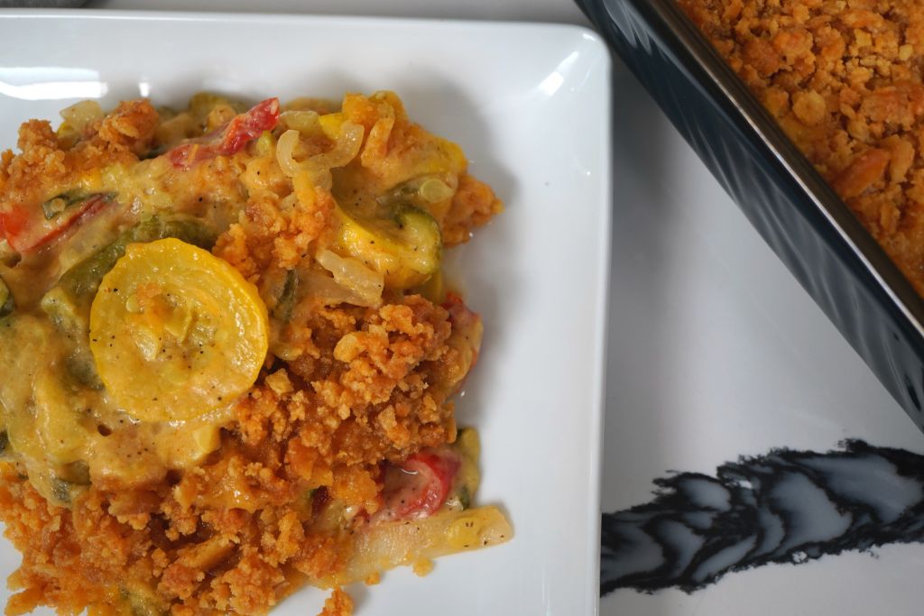A plate of orange-colored rice or grain dish with vegetables and a yellow squash slice.