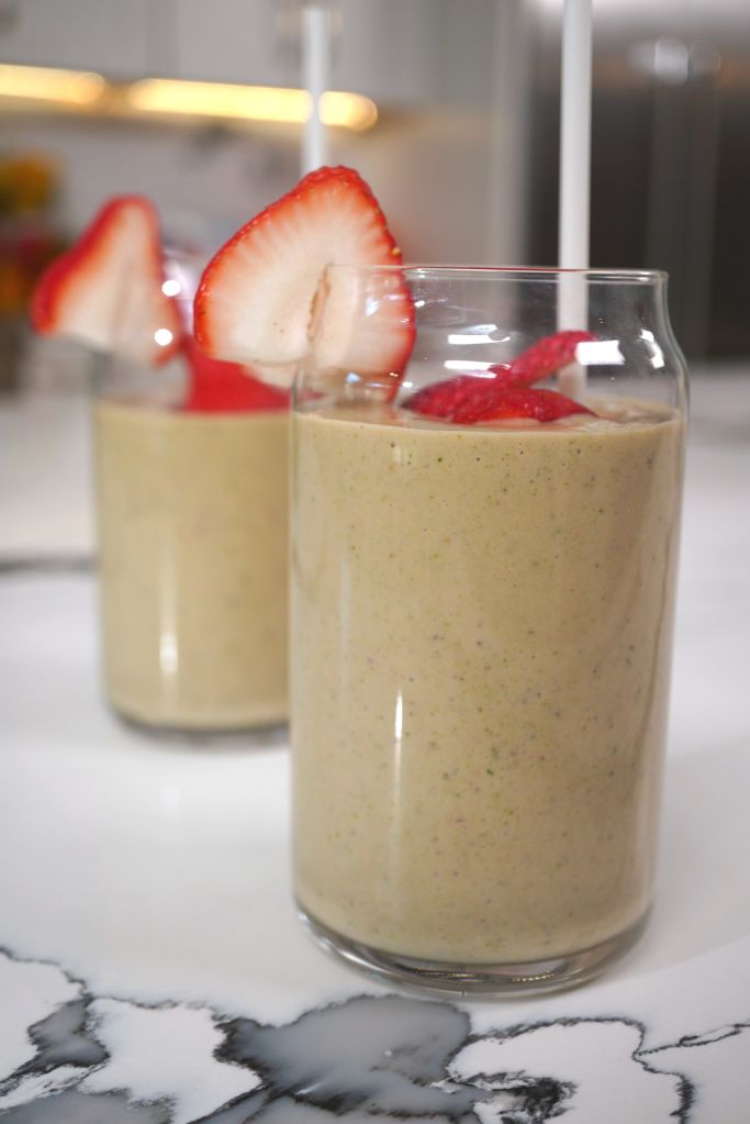 Two glasses of a creamy, yellow smoothie garnished with fresh strawberry slices.