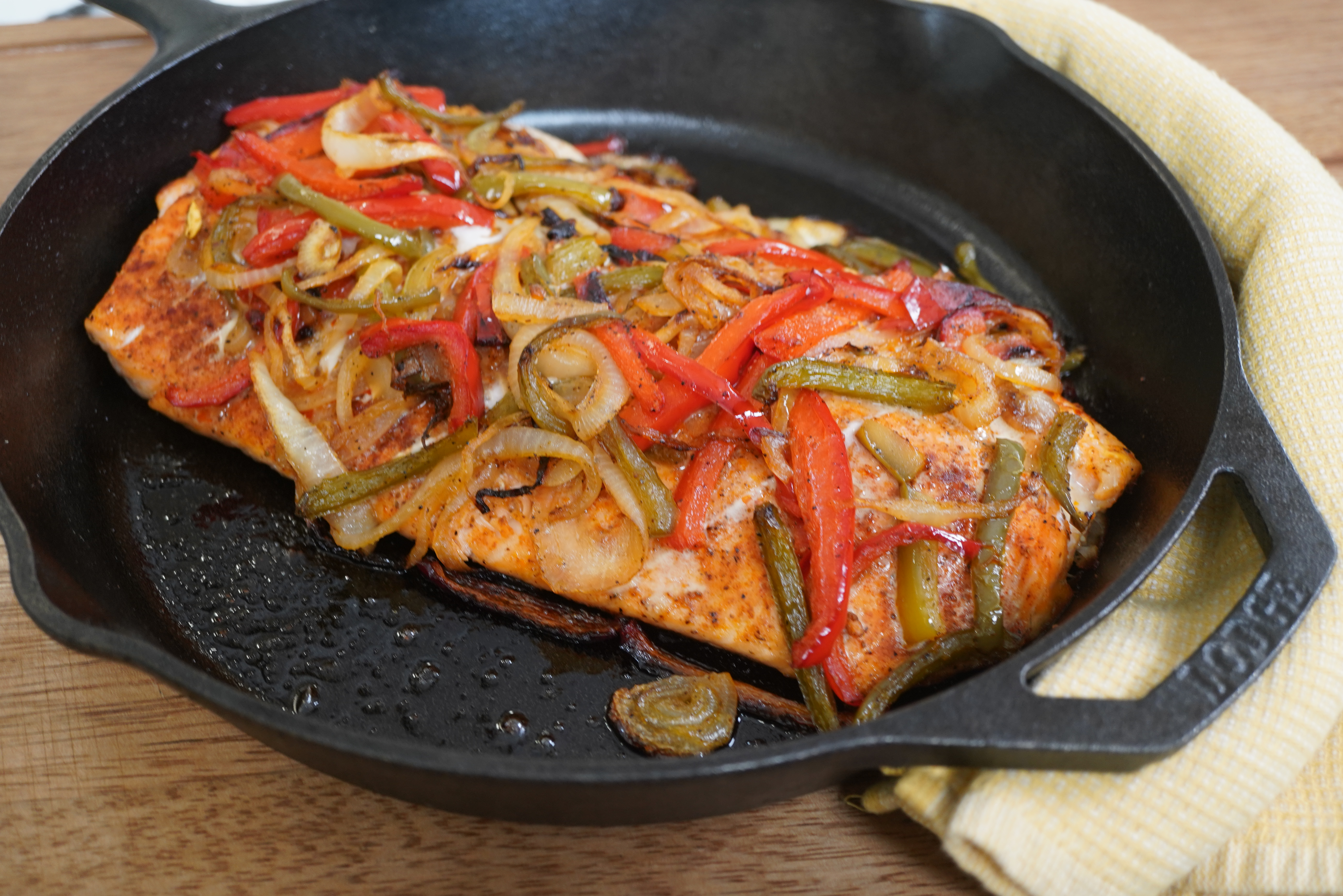 A cast iron skillet filled with sautéed vegetables and a piece of salmon, creating a colorful and flavorful dish.