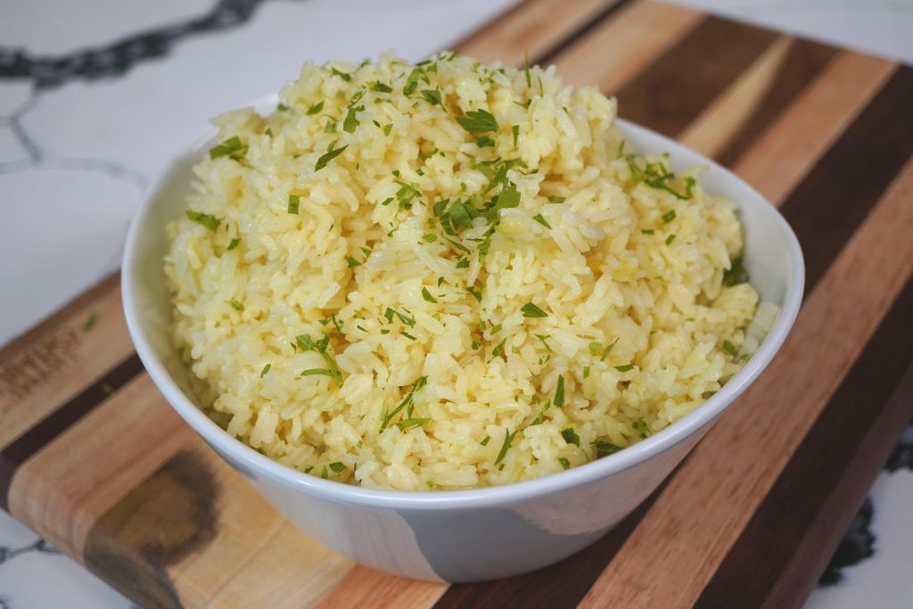 A bowl of fluffy, yellow rice garnished with chopped green herbs.