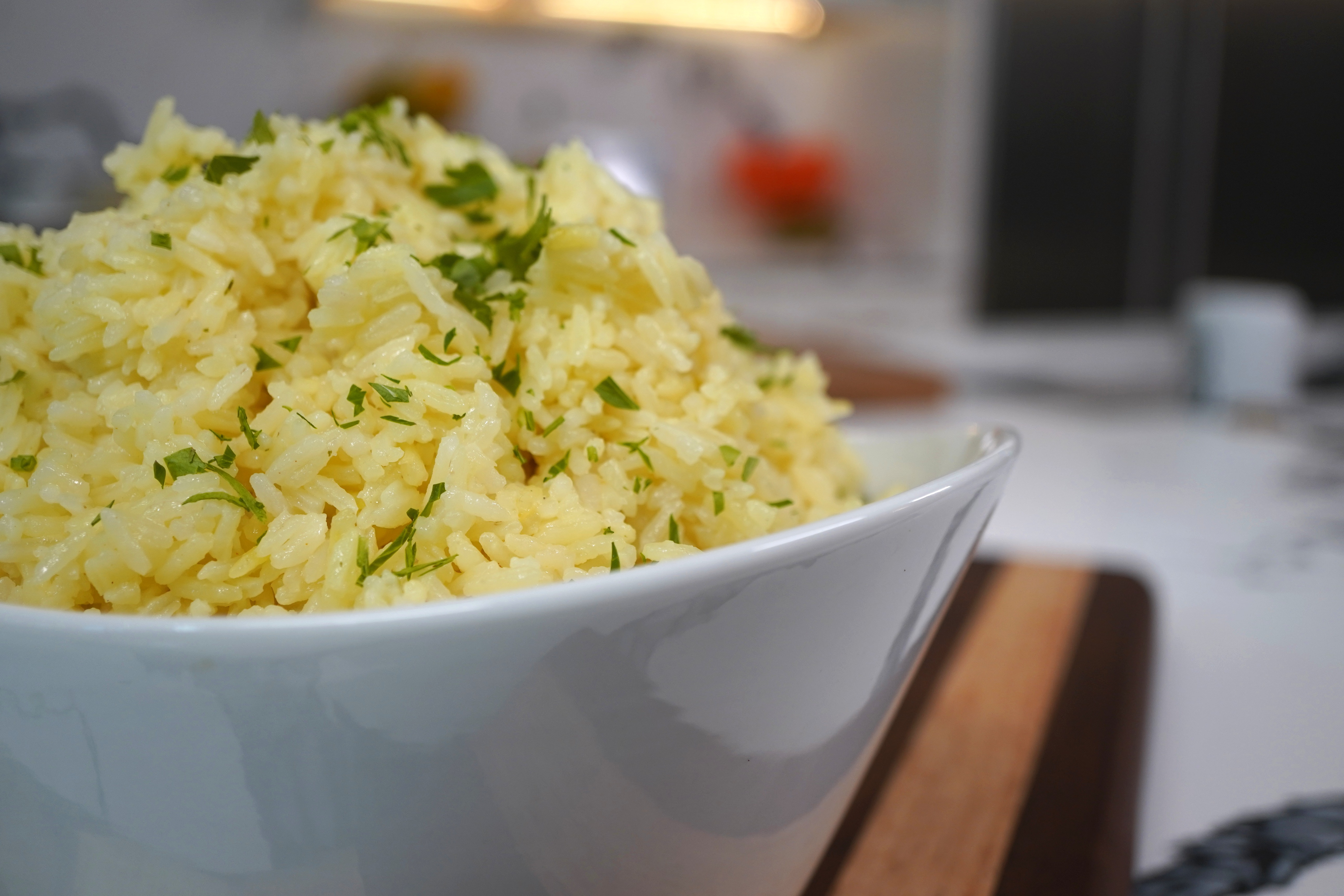 A bowl of fluffy, yellow rice garnished with fresh green herbs.