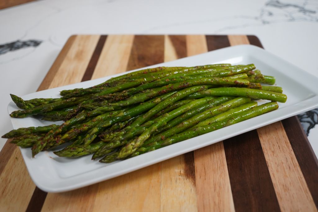 Plate of roasted green asparagus spears on a wooden cutting board.