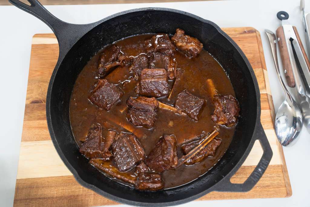 A cast iron skillet filled with a hearty beef stew, with chunks of tender meat and a rich, savory sauce.