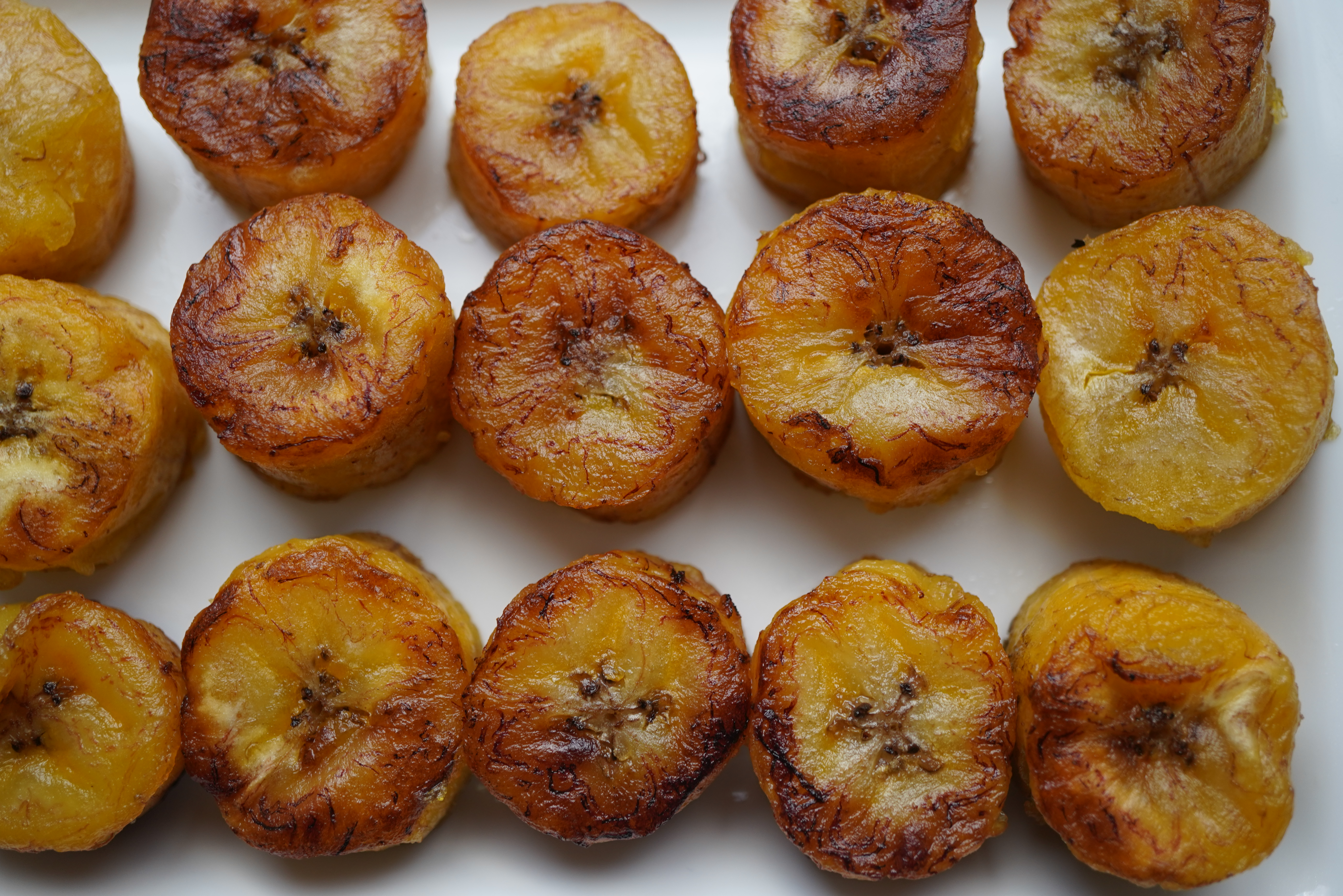 Assorted fried plantain slices on a white surface, with varying degrees of caramelization and browning.