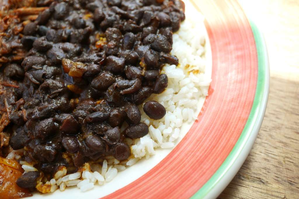 A plate of white rice topped with a dark, savory bean dish.