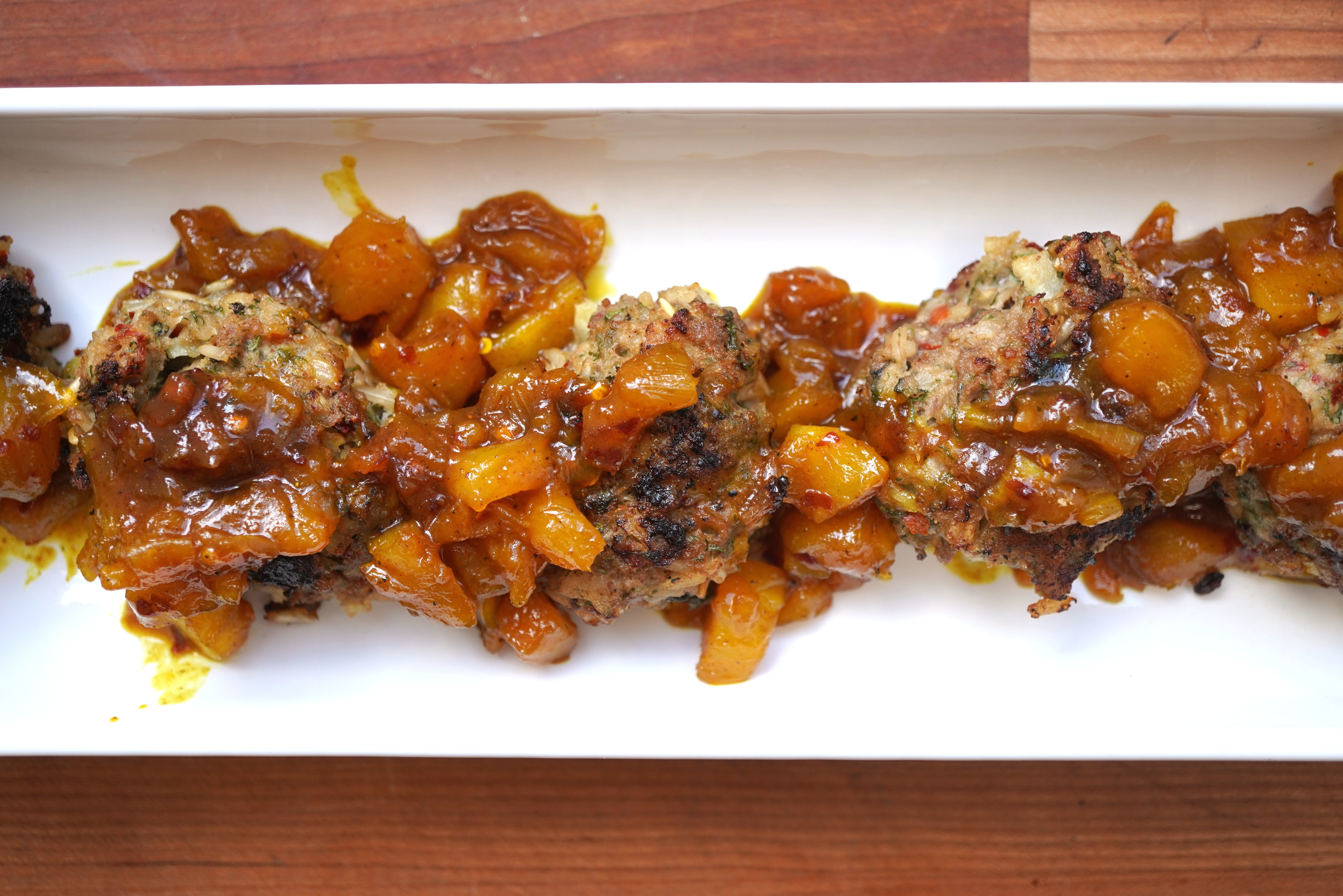 A plate of savory meatballs and roasted vegetables in a rich, caramelized sauce.