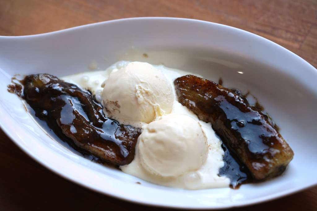 A white plate with two scoops of ice cream and two grilled, caramelized banana slices drizzled with a dark, glossy sauce.