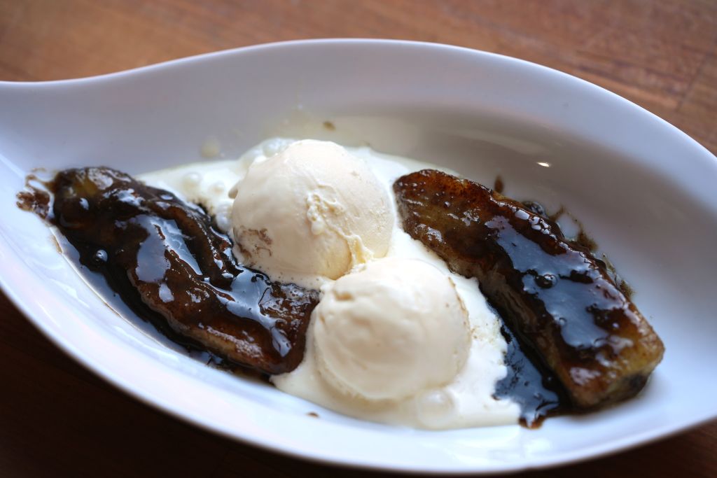 A white plate with two scoops of ice cream and two grilled, caramelized banana slices drizzled with a dark, glossy sauce.